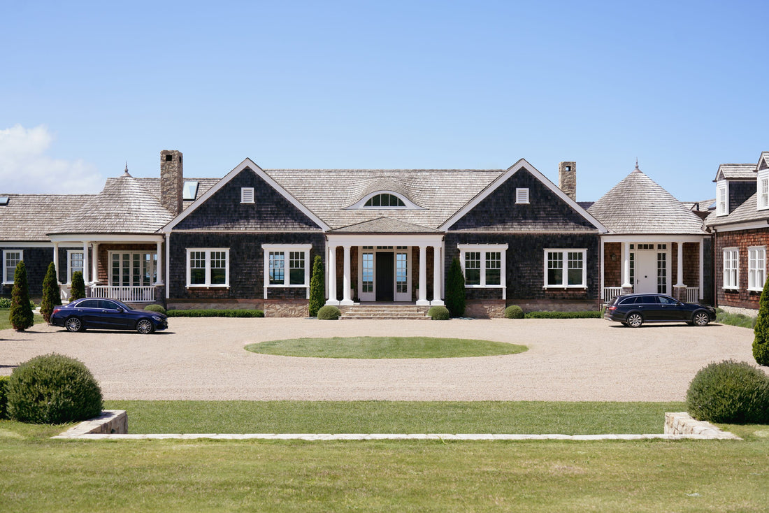 Large two-story house with a driveway and cars in front on a clear day.